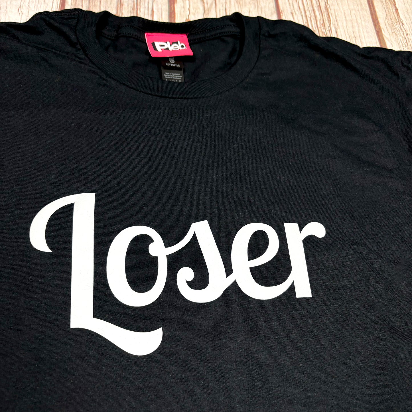 Black t-shirt with 'Loser' in white text on a wooden surface
